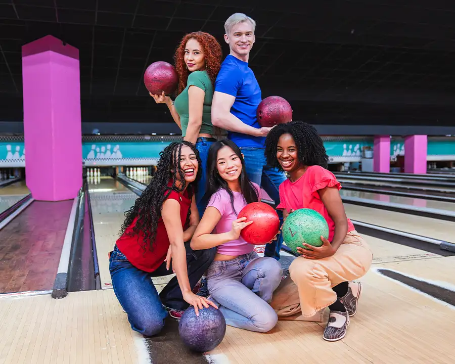 Group of friends posing with bowling balls on pink-lit lanes at Championship Lanes in Anderson, IN